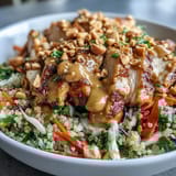 Close-up of sliced, baked chicken over brown rice, topped with crisp carrots, red bell peppers, and shredded purple cabbage in a Peanut Chicken Power Bowl.