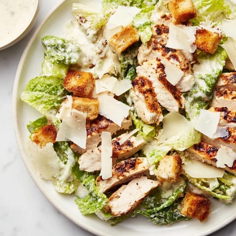 Savory croutons and shaved Parmesan cheese add crunch and richness to the salad. A close-up view of a freshly prepared Chicken Caesar Salad.