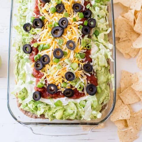 Seven-Layer Dip with refried beans, guacamole, and sour cream, served chilled with tortilla chips for dipping.