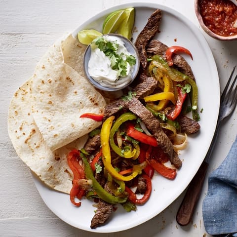 Tender marinated steak and sautéed vegetables for Steak Fajitas, garnished with fresh lime wedges and cilantro on a platter.