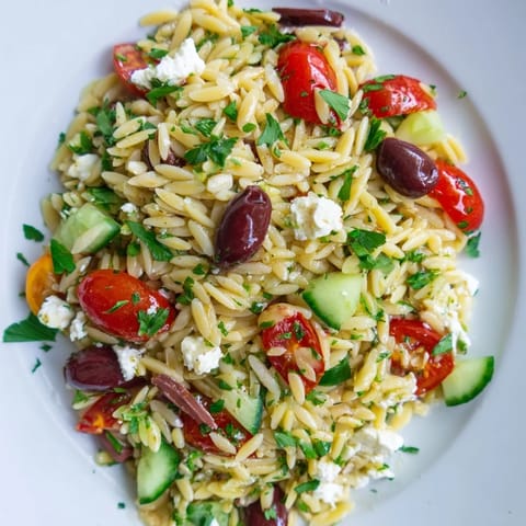 Freshly prepared Greek Orzo Salad in a white bowl, featuring briny Kalamata olives, diced red onion, and herbs, ready for a summer picnic or potluck.