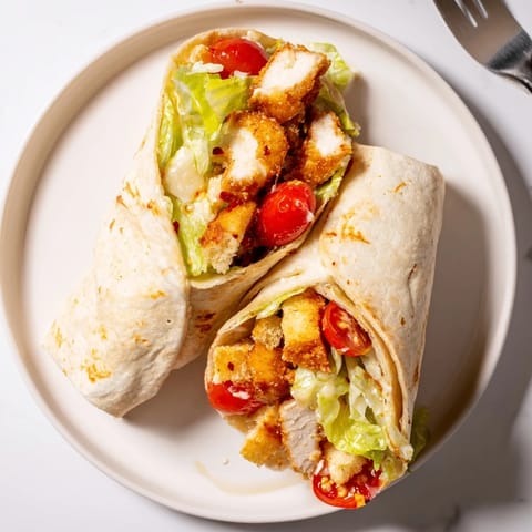 Golden-brown crispy chicken strips coated in spicy hot honey nestled in a warm flour tortilla with creamy Caesar salad.