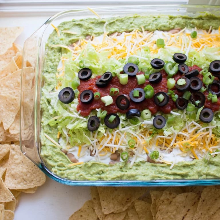 Colorful Tex-Mex Seven-Layer Dip featuring cheddar, salsa, olives, and crisp lettuce for a party appetizer.