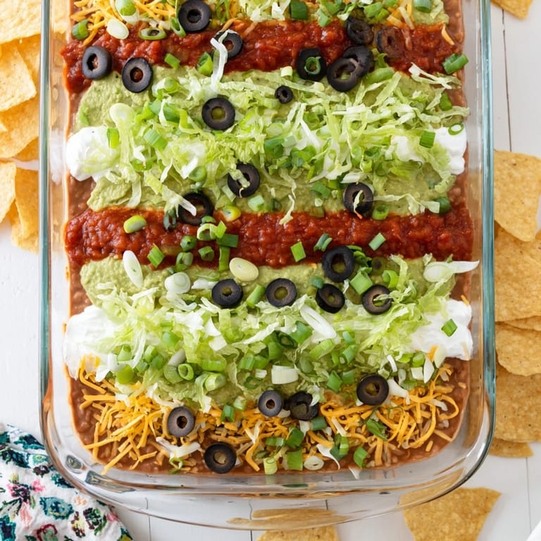 Freshly made Seven-Layer Dip with avocado, cheeses, and green onions, ready to enjoy with crunchy tortilla chips.