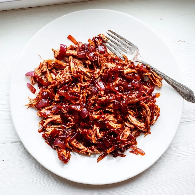 Tender BBQ Pulled Chicken rests in a bowl, garnished with fresh parsley for a bright finish.