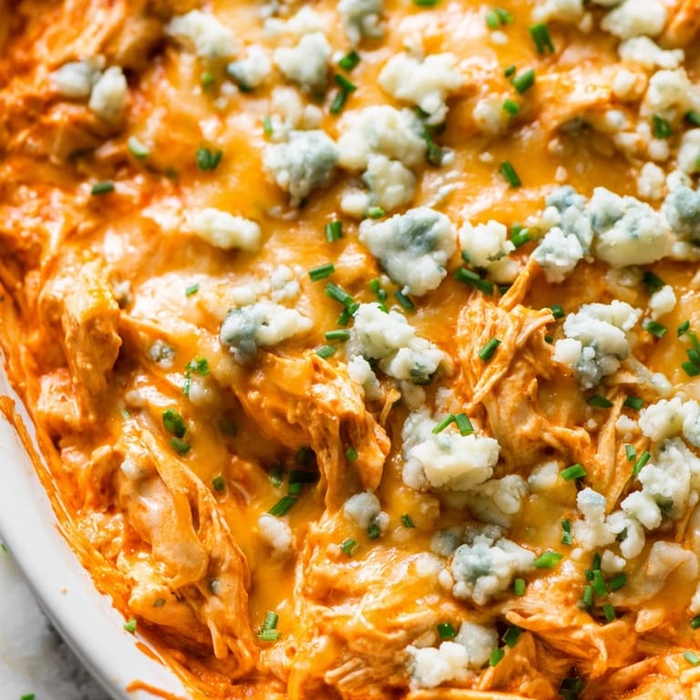 Creamy Buffalo Chicken Dip in a white baking dish, featuring a golden, bubbly cheese crust and chopped green onions. 