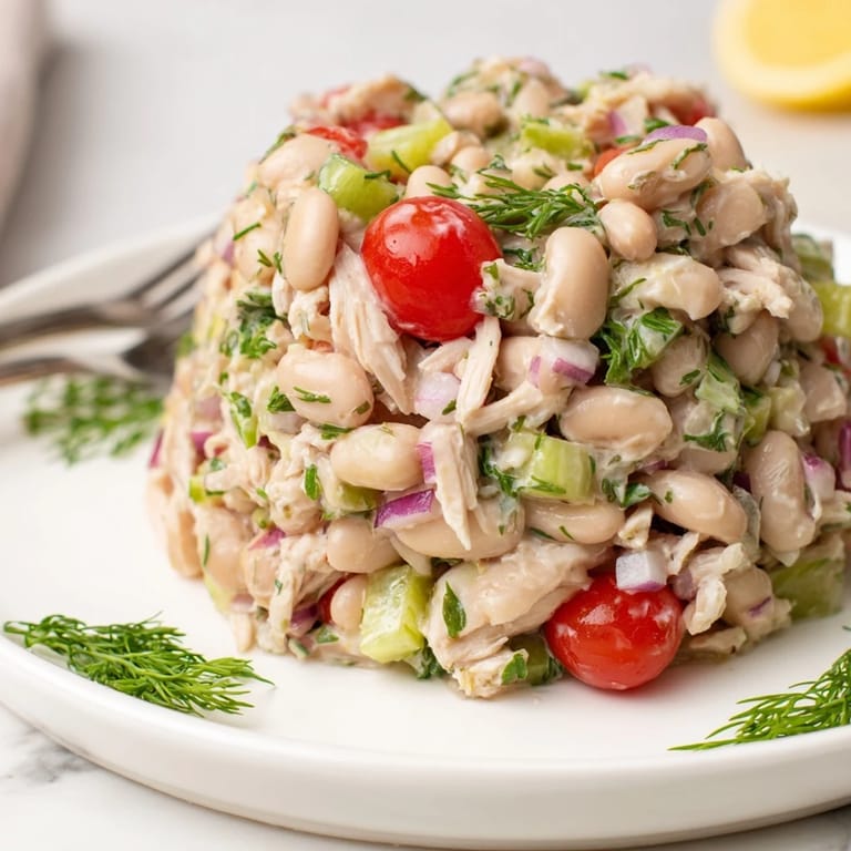 Close-up view of Lemony White Bean Chicken Salad showing juicy cherry tomatoes, red onion, and parsley flakes tossed in a bright olive oil dressing.