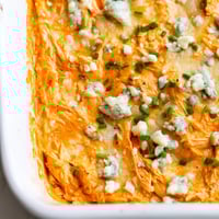 Golden, bubbly Buffalo Chicken Dip fresh from the oven, garnished with chives and ready to serve with celery sticks. 