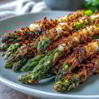 Golden baked Crispy Asparagus Asiago Spears with crunchy panko and melted Asiago, garnished with fresh parsley and served beside lemon wedges for squeezing.  